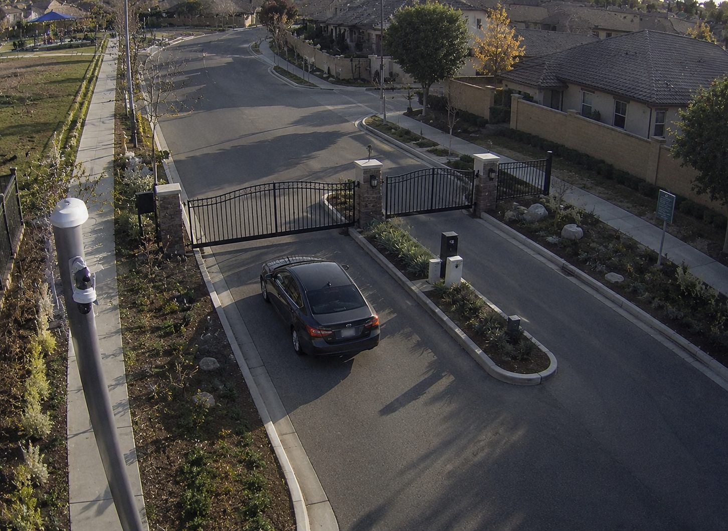 A gated residential entrance at dusk, an SUV waiting at the boom barrier beside a stone guard booth.
